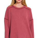 A burgundy ribbed boat neck top. The top has long sleeves, a relaxed fit, and raw edge details on the seams.