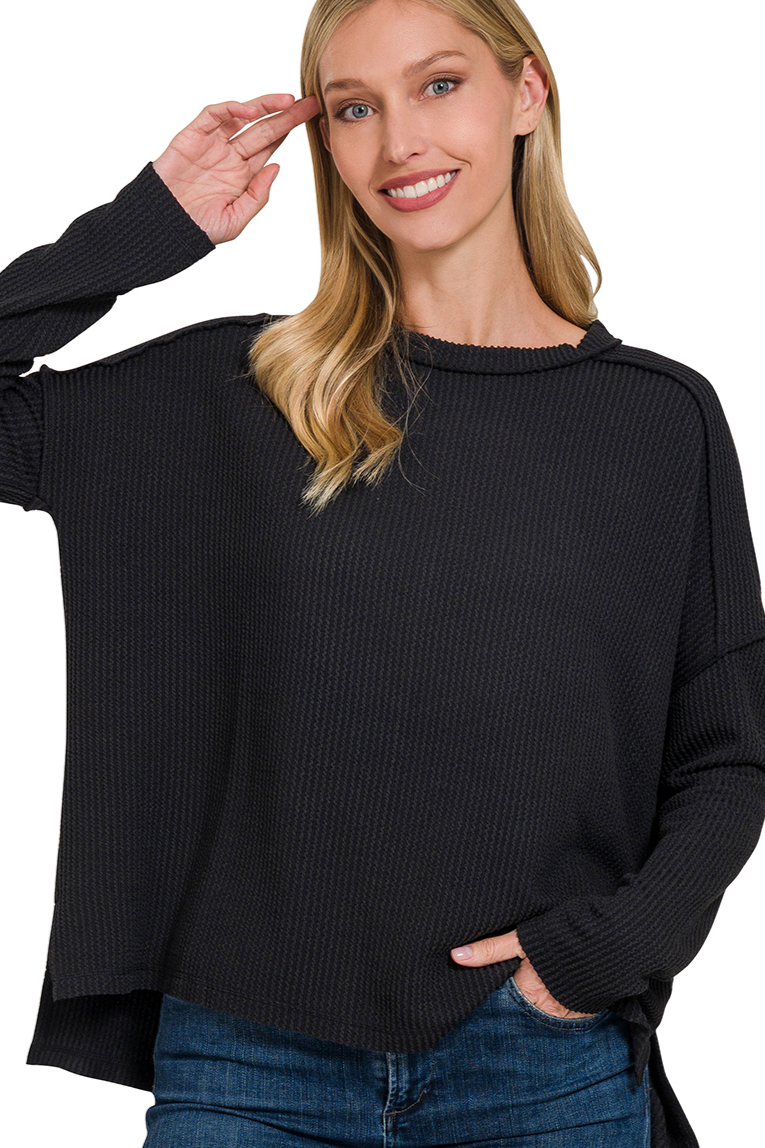 A black ribbed boat neck top. The top has long sleeves, a relaxed fit, and raw edge details on the seams.