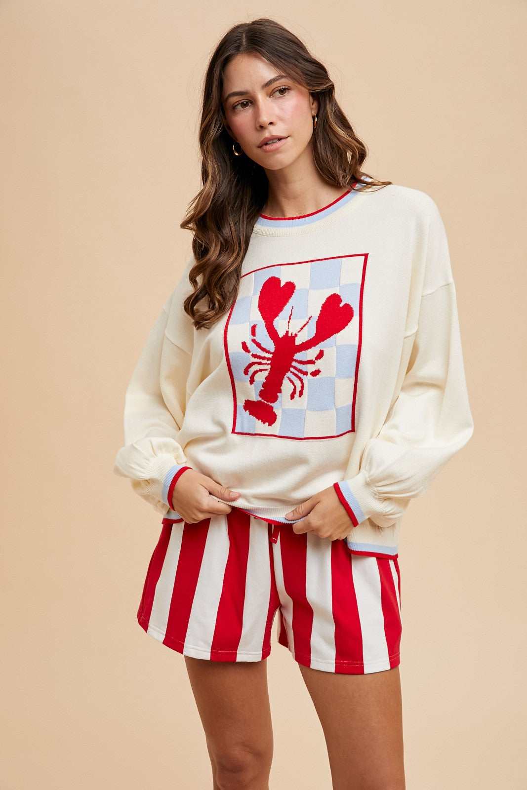 Cream long-sleeve sweater with a large red checkerboard lobster graphic and red striped trim.