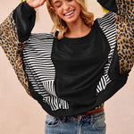 Woman wearing a black and white striped sweater with leopard print sleeves against a beige background