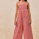 A pair of overalls with a red and white checkerboard plaid print. The overalls have adjustable straps, front pleats, and a wide-leg silhouette.