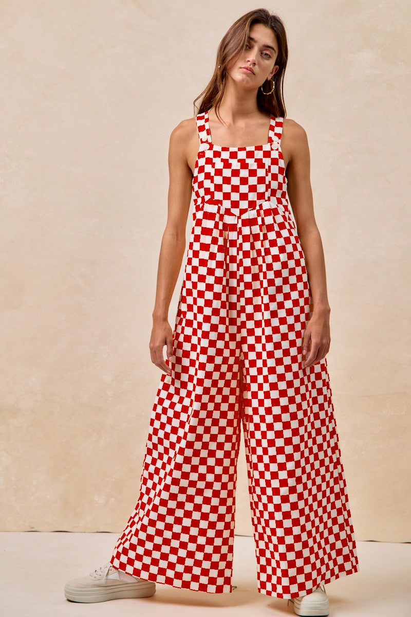 A pair of overalls with a red and white checkerboard plaid print. The overalls have adjustable straps, front pleats, and a wide-leg silhouette.