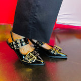 Black pointed-toe flats with bold silver double buckle straps and a slingback backstrap, combining vibrant color with edgy charm.