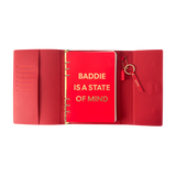 Red notebook with gold text 'BADDIE IS A STATE OF MIND'