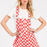 Red checkered knit romper overalls with adjustable straps, metal hardware, multiple pockets, and cuffed shorts, laid flat to highlight color and texture.