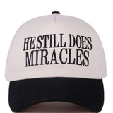 Black and white two-tone cap with “He Still Does Miracles” embroidered on the front.