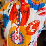 Close-up of the Sicily Calls Dress fabric showing the intricate summer print, partial button-down front, and ruched collar detail, made from breathable cotton with stretch.