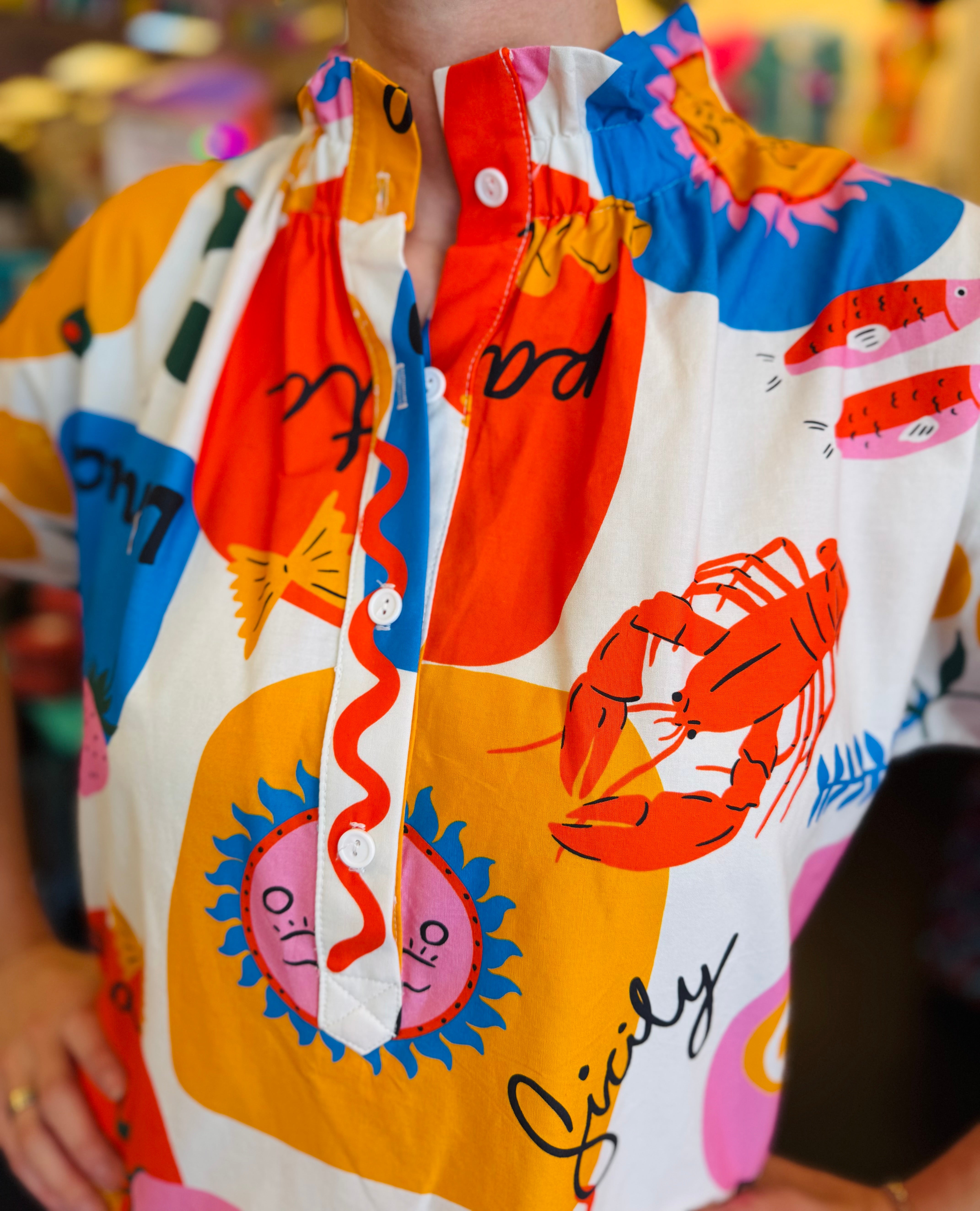 Close-up of the Sicily Calls Dress fabric showing the intricate summer print, partial button-down front, and ruched collar detail, made from breathable cotton with stretch.
