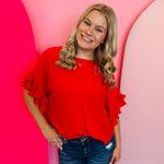A vibrant red woven top featuring dramatic, multi-tiered pleated ruffle sleeves.