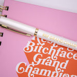 Pen that has “Resting Bitchface Grand Champion,” in gold lettering on a white pen.