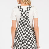 Black checkered knit romper overalls with cuffed shorts, chest and side pockets, and adjustable straps, laid flat to show texture and structure.