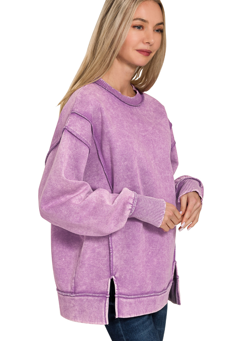 A relaxed-fit, violet acid wash fleece sweatshirt. The sweatshirt has visible exposed seams and a side slit at the bottom.