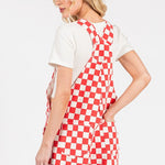 Red checkered knit romper overalls with adjustable straps, metal hardware, multiple pockets, and cuffed shorts, laid flat to highlight color and texture.