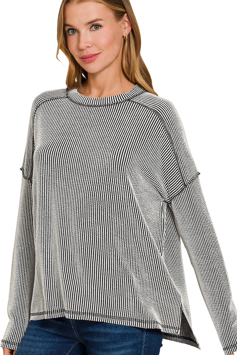 A black and white two-tone ribbed boat neck top. The top has long sleeves, a relaxed fit, and raw edge details on the seams.