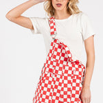 Red checkered knit romper overalls with adjustable straps, metal hardware, multiple pockets, and cuffed shorts, laid flat to highlight color and texture.