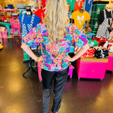 Vibrant floral print top in pink, orange, purple, and green with puff sleeves, round neckline, and contrast trim.