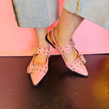 Pink pointed-toe flats with bold silver double buckle straps and a slingback backstrap, combining vibrant color with edgy charm.