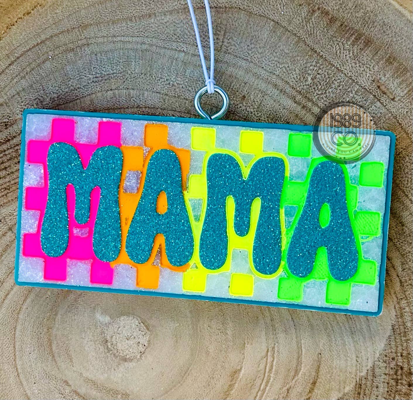 Checkered Rainbow Mama car freshie with blue glitter lettering and border on colorful checkered background.