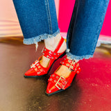 Red pointed-toe flats with bold silver double buckle straps and a slingback backstrap, combining vibrant color with edgy charm.