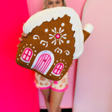 Gingerbread house pillow with frosting details and pink candy accents, soft festive holiday decor.