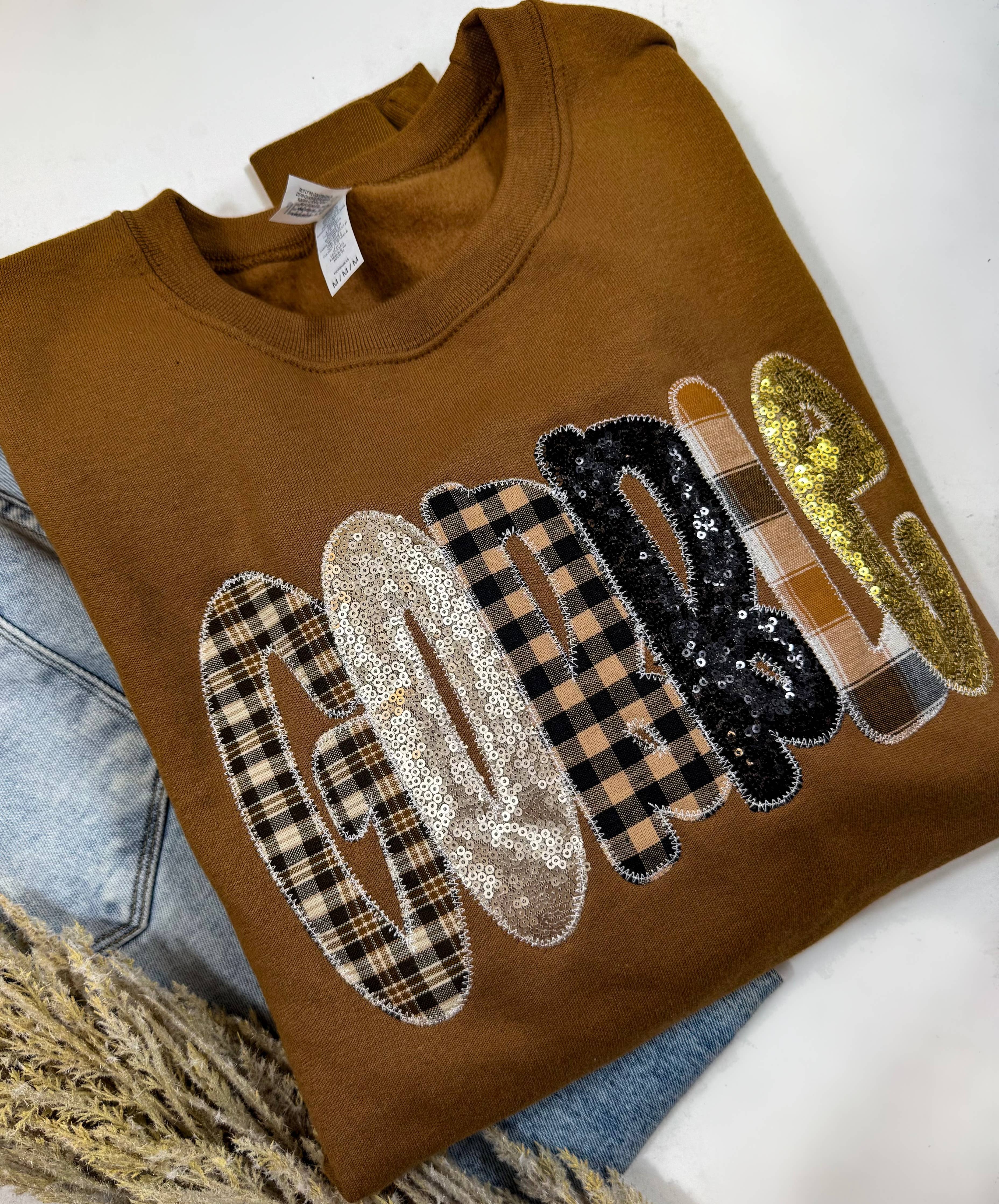 Mocha sweatshirt with plaid and sequin “GOBBLE” letters in warm gold, black, and beige.