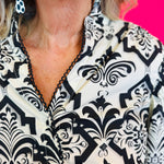 Structured collar and neckline with decorative trim detail against black damask print.