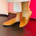 Camel-colored slide sandals with sleek silhouette and spikey stud embellishments along the edge