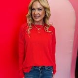 Red ribbed boat neck top with raw edge detailing, long sleeves, and relaxed fit.
