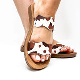 Brown cow print Corkys Wishy Washy sandals featuring playful crisscross straps, cushioned footbed, and a comfortable, modern slip-on design perfect for casual summer wear.