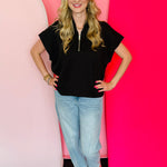 Black scuba high neck top with half zip, displayed folded and styled with denim for a casual-chic look.