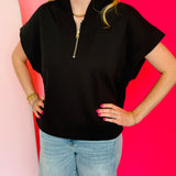 Black scuba high neck top with half zip, displayed folded and styled with denim for a casual-chic look.