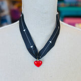 A black scarf necklace with delicate white patterns, accented by a bold red heart charm for a striking contrast. A lightweight, stylish piece perfect for adding a pop of personality to any outfit.