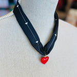 A black scarf necklace with delicate white patterns, accented by a bold red heart charm for a striking contrast. A lightweight, stylish piece perfect for adding a pop of personality to any outfit.