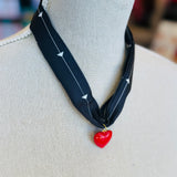 A black scarf necklace with delicate white patterns, accented by a bold red heart charm for a striking contrast. A lightweight, stylish piece perfect for adding a pop of personality to any outfit.