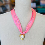 Close-up of a pink printed scarf-style necklace featuring a gold heart charm with a smooth white stone center, styled on a white background for a soft and elegant presentation.