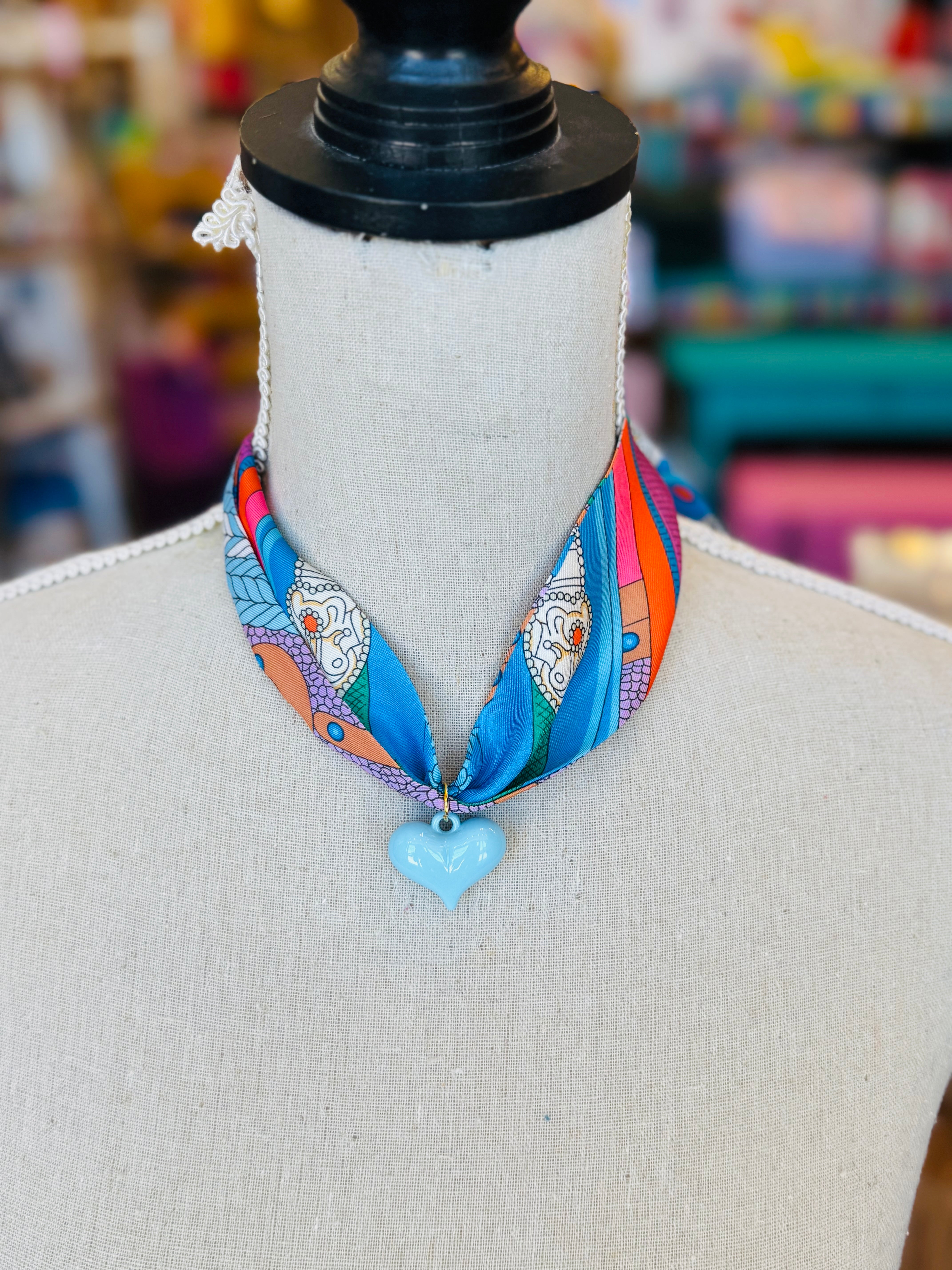 Blue printed scarf necklace featuring a glossy baby blue heart charm; playful and lightweight accessory perfect for adding color and charm to any outfit.