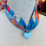 Blue printed scarf necklace featuring a glossy baby blue heart charm; playful and lightweight accessory perfect for adding color and charm to any outfit.