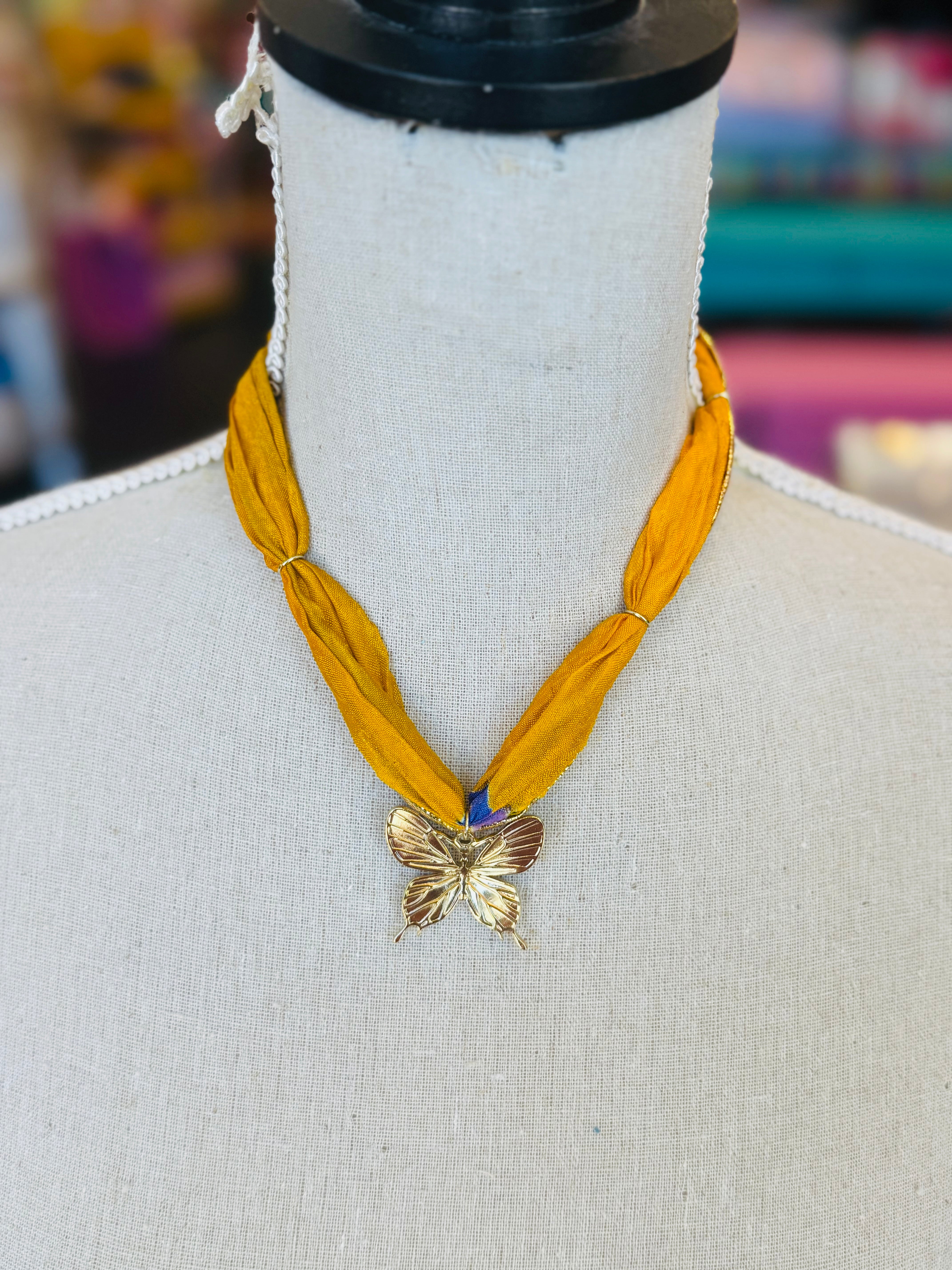 Gold print scarf necklace featuring a delicate gold butterfly charm; a whimsical and stylish accessory perfect for adding elegance and playful charm to any outfit.