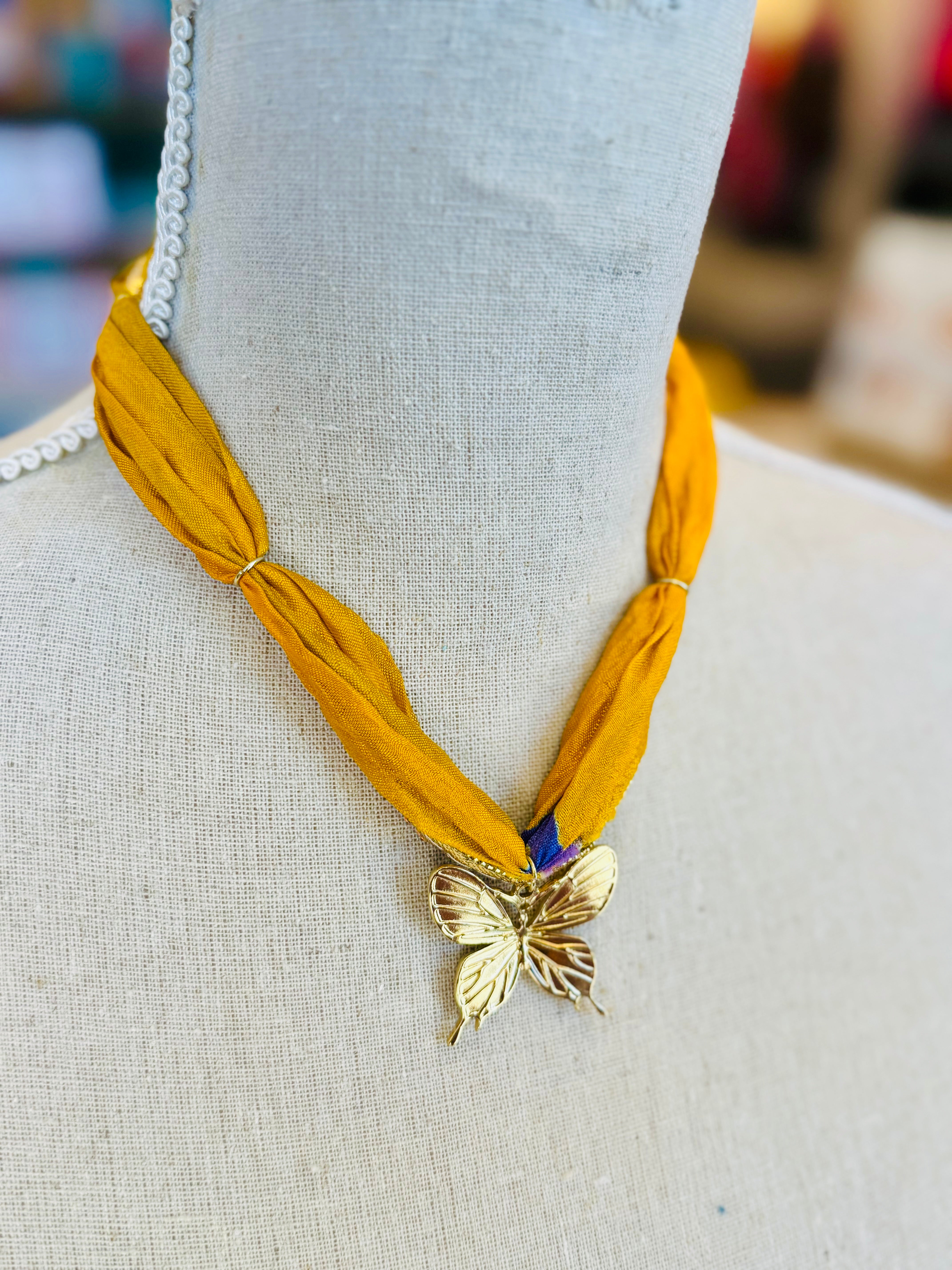 Gold print scarf necklace featuring a delicate gold butterfly charm; a whimsical and stylish accessory perfect for adding elegance and playful charm to any outfit.