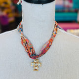 Scarf necklace featuring a richly patterned fabric band and a sculpted gold cross charm with sparkling crystal accents, styled to add vintage charm and elegance to any outfit.