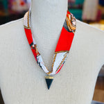 Red patterned scarf necklace featuring a sleek black triangle pendant with gold trim, styled to add a bold yet elegant statement to any outfit.