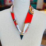 Red patterned scarf necklace featuring a sleek black triangle pendant with gold trim, styled to add a bold yet elegant statement to any outfit.