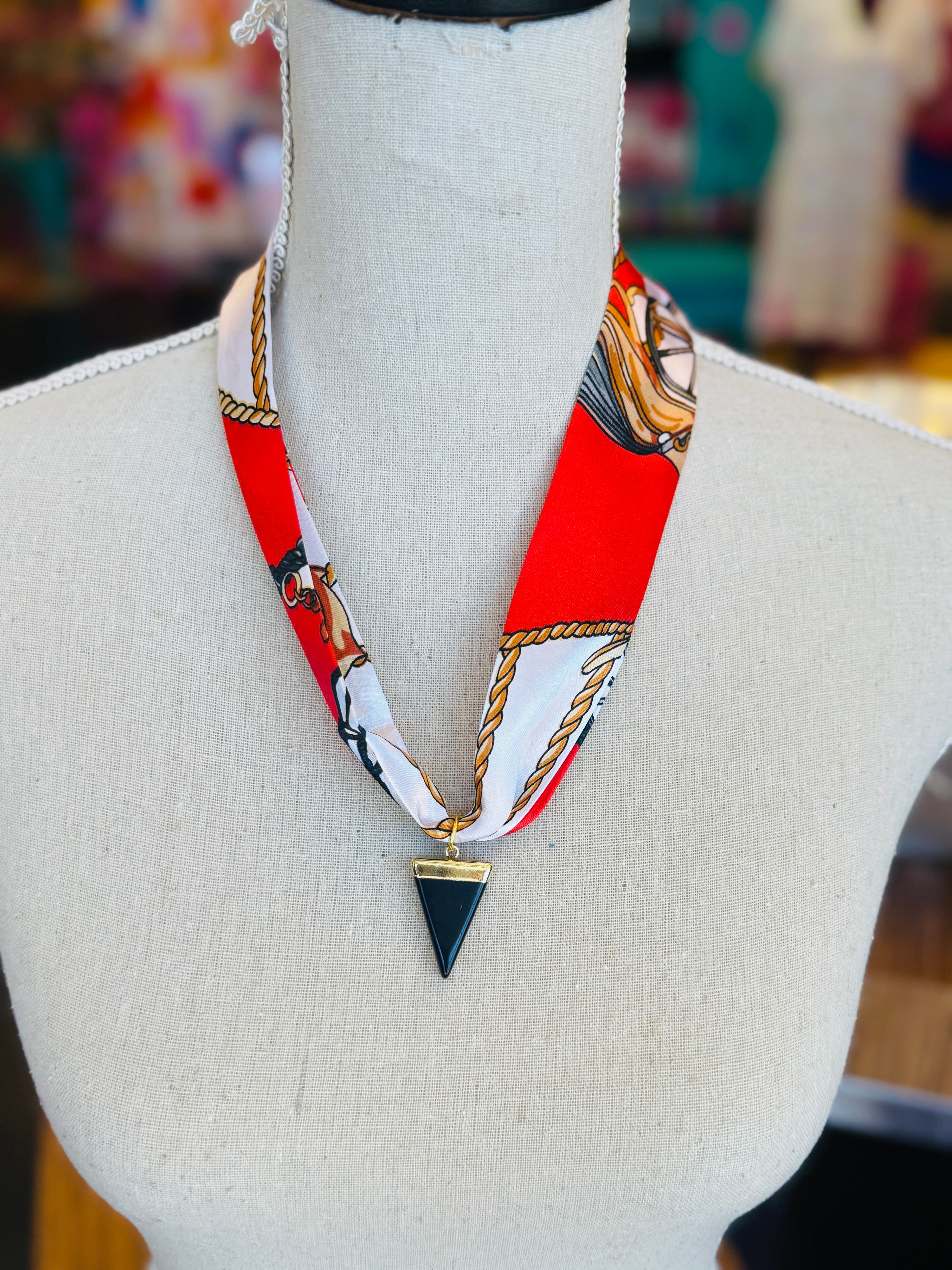 Red patterned scarf necklace featuring a sleek black triangle pendant with gold trim, styled to add a bold yet elegant statement to any outfit.