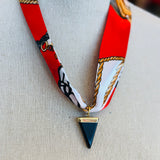 Red patterned scarf necklace featuring a sleek black triangle pendant with gold trim, styled to add a bold yet elegant statement to any outfit.