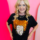 A black crewneck t-shirt featuring a glittery orange witch hat graphic. Below the hat, the text reads, "It's Just a Bunch of Hocus Pocus" in a stylized font.