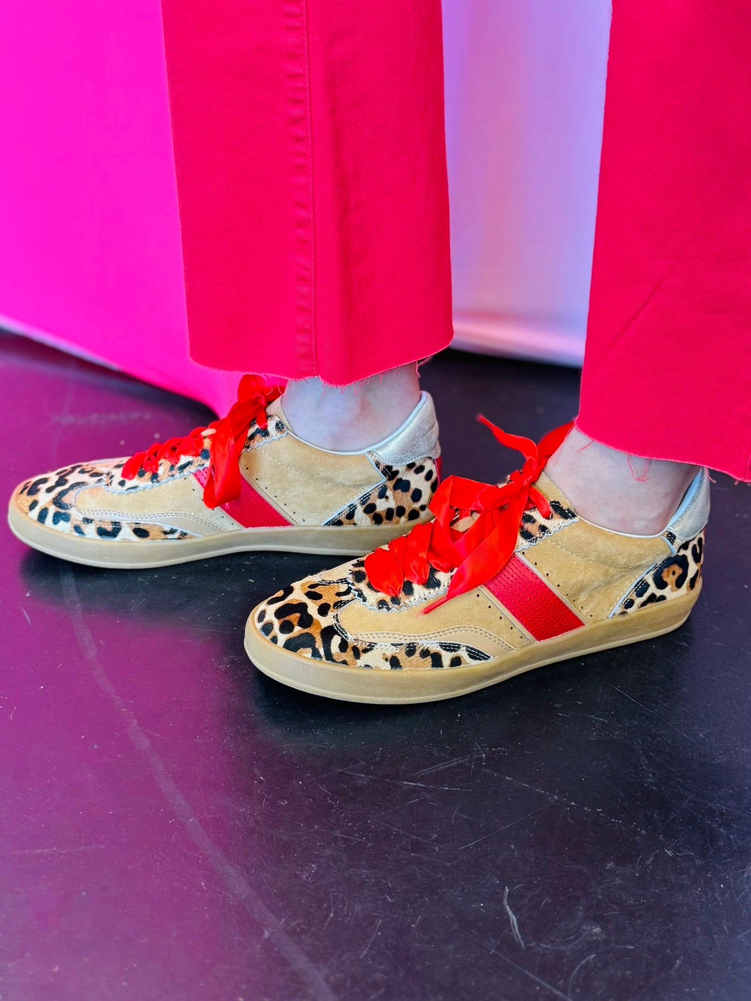 Leopard suede sneakers with red stripe, red laces, and gold heel accent.