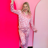 two piece button up pink satin pajama set with long-sleeve button-up top and pants and small red candy canes and bows.