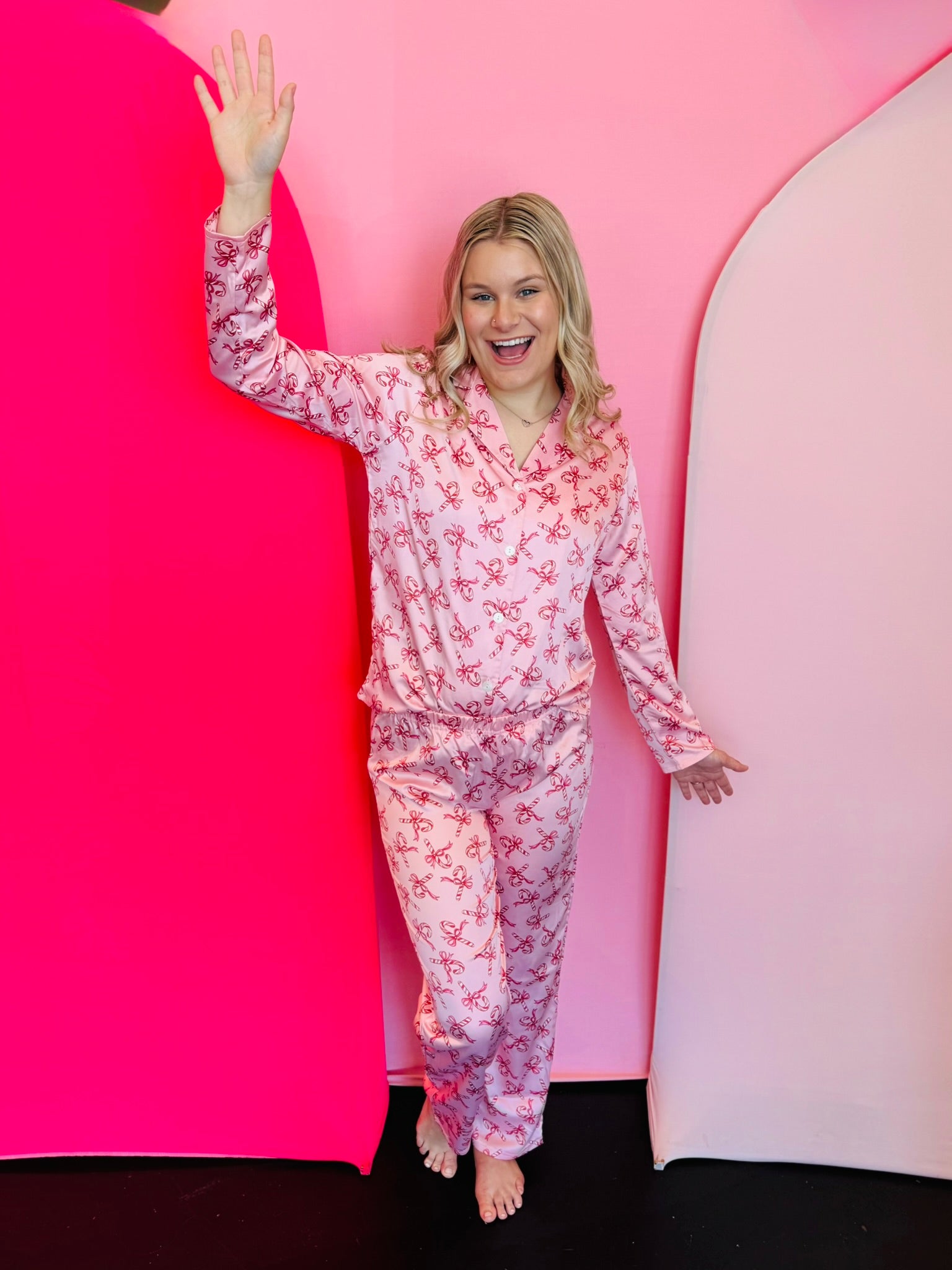 two piece button up pink satin pajama set with long-sleeve button-up top and pants and small red candy canes and bows.