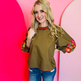 Olive embroidery top with red trim, floral sleeves, and ruffled mock neck.