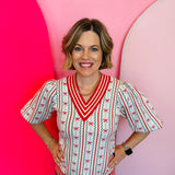 Cream colored sweater with red striped v-neck, sleeves, and hemline. Bow and zig zag pinstripe design.